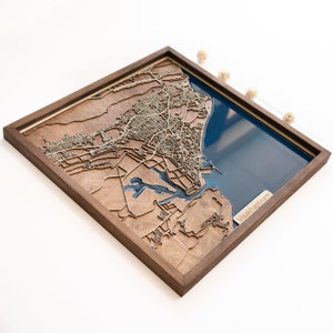 May include: A wooden, layered map of Visakhapatnam, India, framed in a dark brown wood. The map features intricate laser-cut details of the city's layout, with a blue resin representing the coastline and water bodies. The text "Visakhapatnam" is visible.