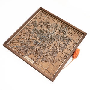 May include: A wooden map of Bend, Oregon, in a walnut frame. The map is laser cut and shows the city's streets and landmarks. The text "Bend, OR" is visible in the lower left corner of the map.