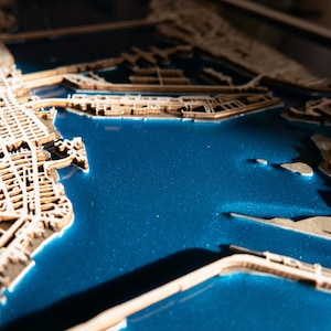 A wooden map of your favourite place enclosed in a wooden frame. It has 3D city streets and epoxy resin water. By adding a pin in a important place for you and an engraving you will make a personalized gift.