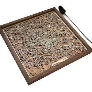 May include: A wooden map of Raleigh, North Carolina, in a walnut frame. The map is laser cut and shows the city's streets and landmarks.