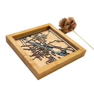 May include: A wooden framed map of a city with blue water features. The map is raised and appears to be laser cut.