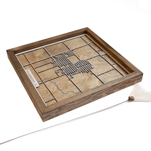 Könnte beinhalten: Eine Holzrahmenkarte von Hoopeston, Illinois, mit einem blauen Fluss und einem Gittermuster. Die Karte ist lasergeschnitten und auf einem Holzgrund montiert.