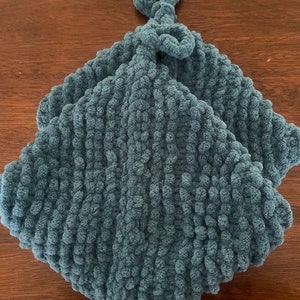 May include: A teal blue crocheted baby blanket with a knotted loop at the top.