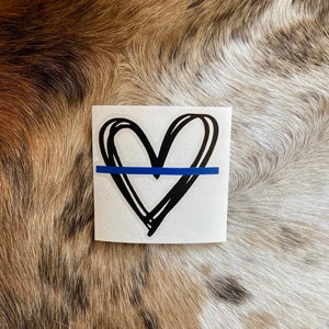 K&ouml;nnte beinhalten: Ein wei&szlig;er Aufkleber mit einem handgezeichneten schwarzen Herzen und einer blauen Linie in der Mitte. Der Aufkleber befindet sich auf einem braunen und wei&szlig;en Fellhintergrund.