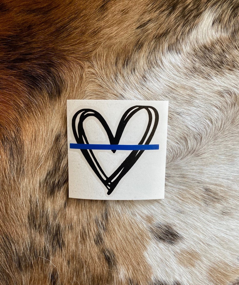 K&ouml;nnte beinhalten: Ein wei&szlig;er Aufkleber mit einem handgezeichneten schwarzen Herzen und einer blauen Linie in der Mitte. Der Aufkleber befindet sich auf einem braunen und wei&szlig;en Fellhintergrund.
