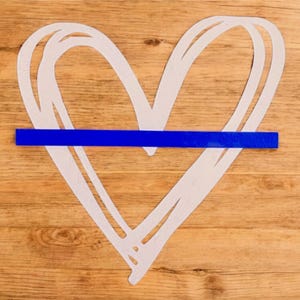 K&ouml;nnte beinhalten: Ein wei&szlig;es Herz, das auf eine Holzoberfl&auml;che gezeichnet ist, mit einer blauen Linie in der Mitte.