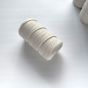 May include: A close-up of a white cotton cord wound into a roll. The cord is thick and has a textured surface.