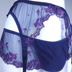 May include: A dark blue garter belt and matching underwear set featuring sheer mesh panels with intricate purple floral embroidery. The garter belt includes adjustable straps and a scalloped edge, while the solid blue fabric provides coverage.
