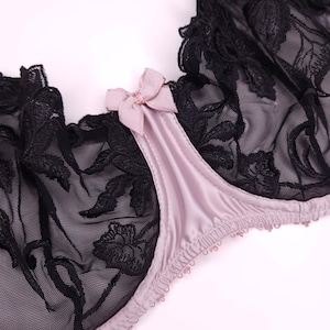 May include: A black lace bra with a pink satin cup and a bow detail. The bra has a floral pattern and is made of delicate fabric.