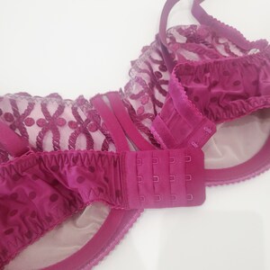 May include: A close-up of the back of a burgundy bra with a lace and polka dot pattern. The bra has an adjustable hook and eye closure.