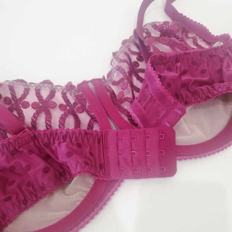 May include: A close-up of the back of a burgundy bra with a lace and polka dot pattern. The bra has an adjustable hook and eye closure.