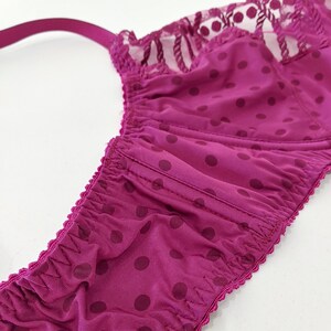 May include: A close-up of a pink bra with a polka dot pattern and a lace trim. The bra has a gathered elastic band at the bottom.