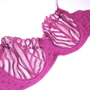 May include: A pink lace bra with a delicate floral pattern. The bra has a scalloped edge and a hook and eye closure.