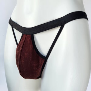 Può includere: Un perizoma bordeaux con finiture nere e una fascia in vita nera. Il perizoma è esposto su un manichino bianco. Il tessuto ha un aspetto strutturato.