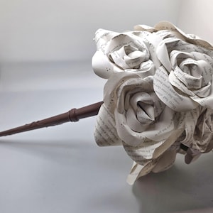 May include: A bouquet of paper roses made from book pages. The white roses are clustered together, with visible text from the book. The stem is a dark brown color.
