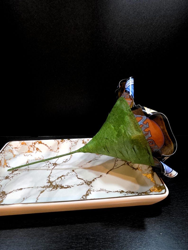 May include: A decorative serving tray with a white marble design and gold accents. A green leaf-shaped object rests on the tray, with a stem extending across the surface. A colorful label is partially visible.