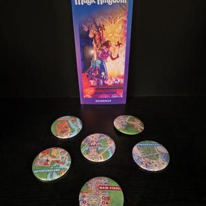 May include: A Magic Kingdom guidemap featuring a colorful illustration of a person with a pinwheel, accompanied by five circular buttons displaying various sections of the park map, including Adventureland, Tomorrowland, and Main Street.