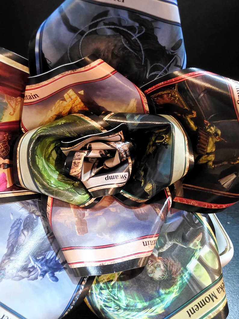 May include: A close-up of a collection of Magic: The Gathering trading card wrappers, rolled and folded to create a layered, abstract design. The wrappers display various fantasy art scenes, including mountains, swamps, and figures, with text labels.