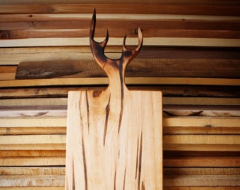 May include: A wooden cutting board with a burnt deer antler handle. The board has a natural wood grain pattern and is rectangular in shape.