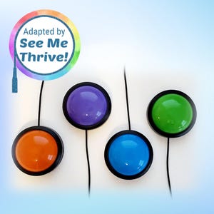 May include: Four colorful, round buttons with black rims and attached wires. The buttons are orange, purple, blue, and green. The image also includes a circular logo with the text "Adapted by See Me Thrive!"