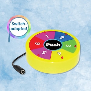 May include: A round, yellow switch-adapted device featuring a central black button labeled Push. The surface is divided into six colorful segments numbered one through six, each with a small red light. A black cable with a jack plug is attached.