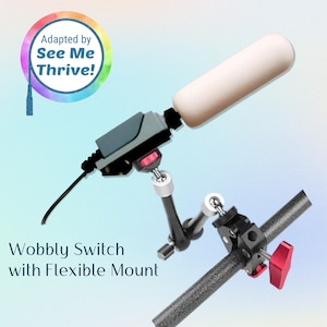 May include: A Wobbly Switch with Flexible Mount, featuring a white cylindrical component and a black and gray control unit. The mount includes a black arm with silver joints and a clamp with a red adjustment knob. The text "Adapted by See Me Thrive!" is in a colorful circle.
