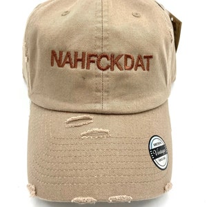 May include: A beige distressed baseball cap with the text "NAHFCKDAT" embroidered in orange on the front. The cap has a vintage label on the back.