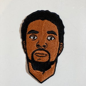 Puede incluir: Parche bordado de la cara de una persona con piel morena, cabello negro y barba. La persona está mirando directamente al espectador.