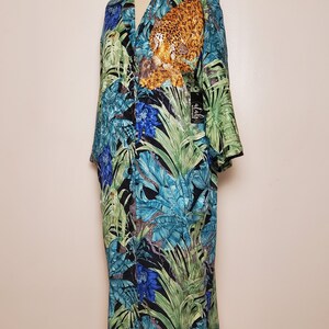 May include: A long-sleeved, button-up shirt with a tropical print featuring a leopard, parrots, and blue flowers. The shirt is on a mannequin and has a black tag that says "alah" on it.