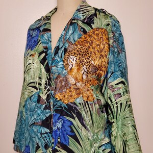 May include: A black silk shirt with a jungle print featuring a leopard, tropical leaves, and blue flowers. The shirt has a button-up front and long sleeves.