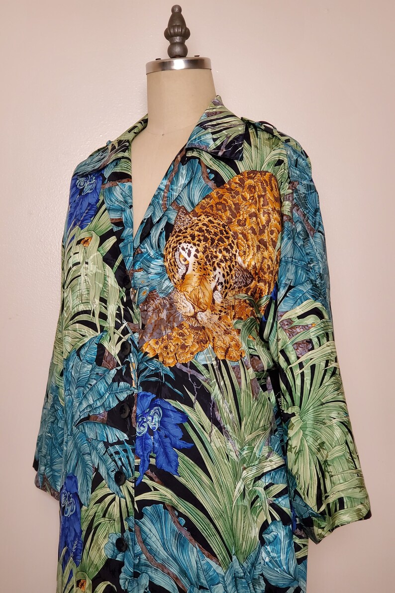 May include: A black silk shirt with a jungle print featuring a leopard, tropical leaves, and blue flowers. The shirt has a button-up front and long sleeves.