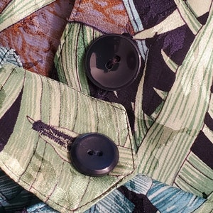 May include: Close-up of two black buttons on a green and black fabric with a tropical leaf pattern.