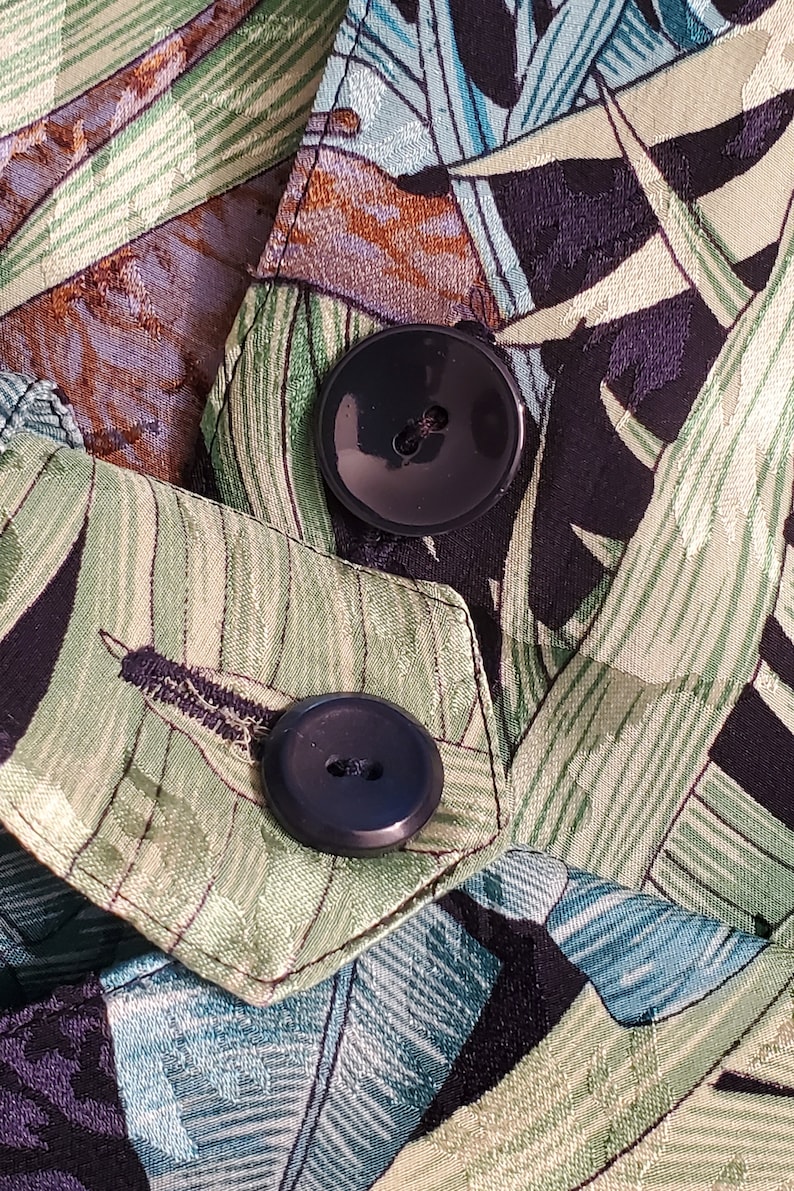 May include: Close-up of two black buttons on a green and black fabric with a tropical leaf pattern.
