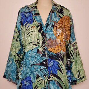 May include: A black button-up shirt with a jungle print featuring a leopard, green leaves, and blue flowers. The shirt has a collar and long sleeves.
