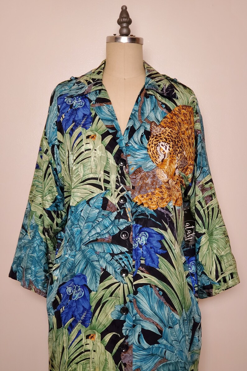 May include: A black button-up shirt with a jungle print featuring a leopard, green leaves, and blue flowers. The shirt has a collar and long sleeves.