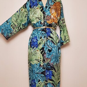 May include: A long-sleeved button-down shirt with a tropical print featuring green leaves, blue flowers, and a leopard. The shirt has a gold belt and is on a white mannequin.