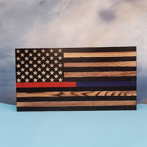 May include: Wooden American flag with a distressed finish. The flag features the traditional stars and stripes, with a red line and a blue line. The stars are light-colored, and the stripes are a mix of dark and light wood.