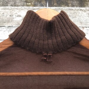 May include: A brown sheer turtleneck sweater with a ribbed knit collar. The sweater has a small embroidered logo on the front.