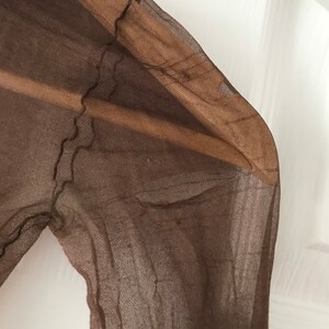 May include: A brown sheer fabric with a textured pattern. The fabric is folded and has a slightly frayed edge.
