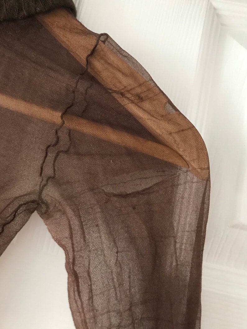 May include: A brown sheer fabric with a textured pattern. The fabric is folded and has a slightly frayed edge.