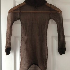 May include: A brown sheer turtleneck sweater with a brown knit collar. The sweater is hanging on a hanger against a white door.