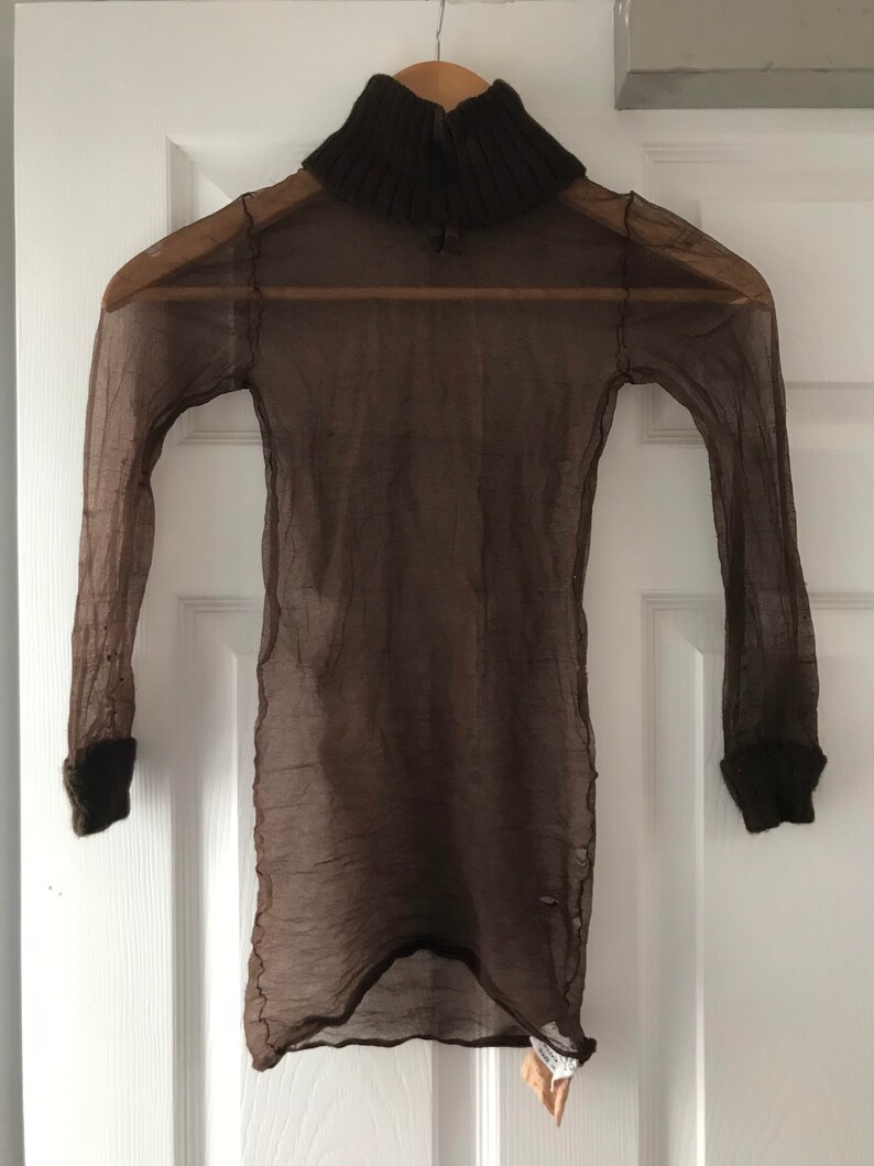 May include: A brown sheer turtleneck sweater with a brown knit collar. The sweater is hanging on a hanger against a white door.