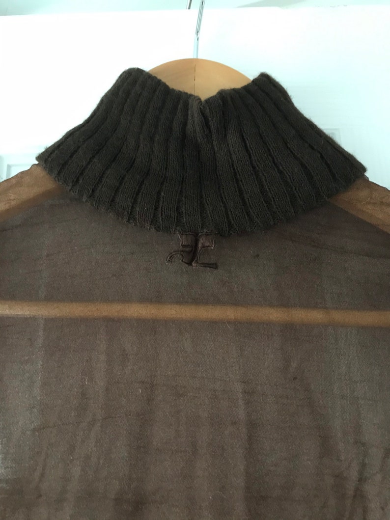 May include: A brown turtleneck sweater with a sheer overlay. The sweater has a ribbed knit texture and a small logo on the back.