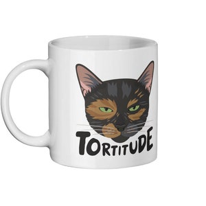 Pode incluir: Caneca de cer&acirc;mica branca com uma ilustra&ccedil;&atilde;o de um gato preto, laranja e marrom e o texto "Torttitude" em preto.