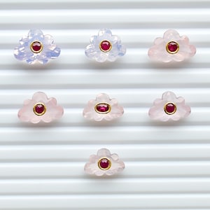 May include: Seven cloud-shaped gemstones arranged in a grid. Each piece features a translucent, pale pink or light blue stone carved into a scalloped cloud form, with a small, round or oval red gemstone set in a gold-toned bezel at the centre.