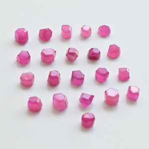 May include: A collection of 20 pink faceted gemstone beads. The beads are arranged in a heart shape on a white background.