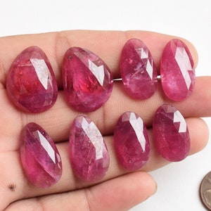 Pode incluir: Sete pedras preciosas de rubi rosa facetadas em forma de lágrima. As pedras preciosas medem aproximadamente 2,5 cm de comprimento e são exibidas em uma mão.