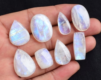 May include: A collection of eight iridescent moonstone cabochons in various shapes and sizes, including teardrop, oval, and rectangular.