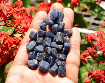 May include: A handful of small, rough, dark blue sapphire crystals. The crystals are faceted and have a natural, unpolished look.