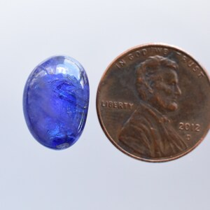 May include: A blue oval gemstone with a faceted surface, next to a US penny for size comparison.